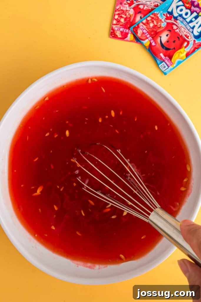 Sweet & Sour Zingers 9 A whisk stirring the mixture of pickle brine and bright red Kool-Aid in a white bowl, ensuring all ingredients are well combined.