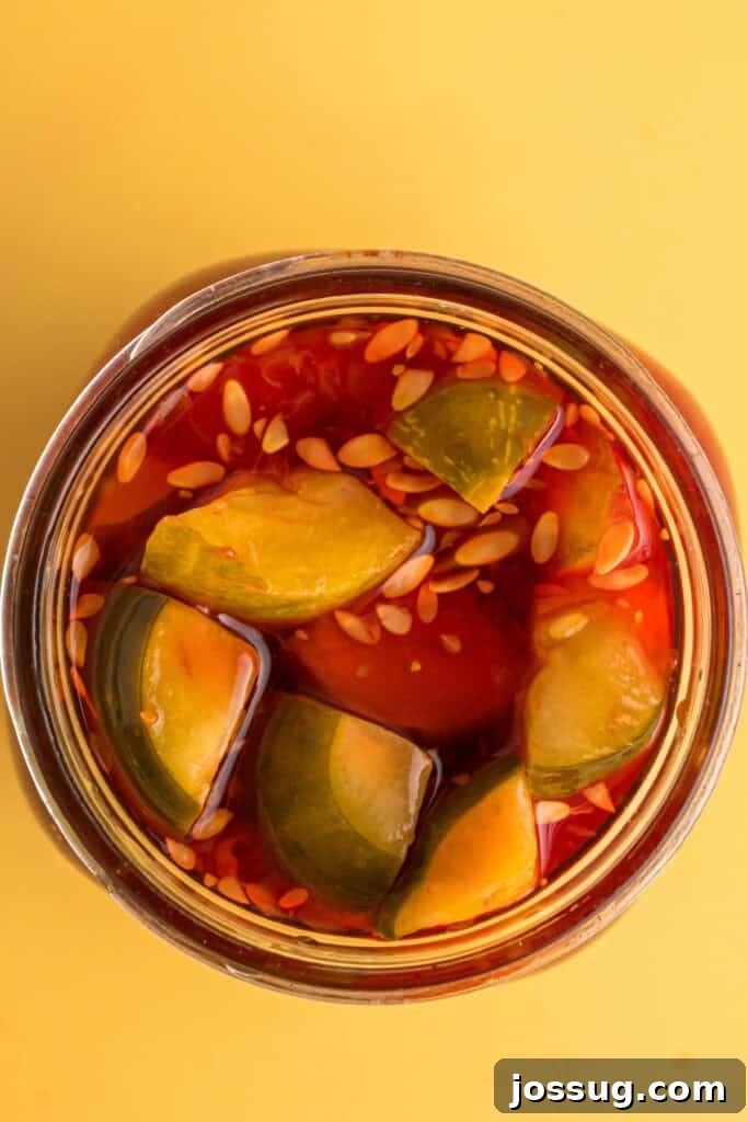 Sweet & Sour Zingers 10 Pickle spears fully submerged in a vibrant red Kool-Aid brine inside a clear glass jar, marinating.