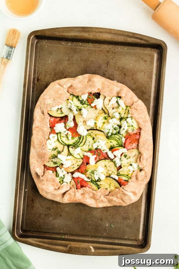 Unbaked summer vegetable galette with neatly folded crust edges, brushed with egg wash, and ready to be placed in the oven for baking.