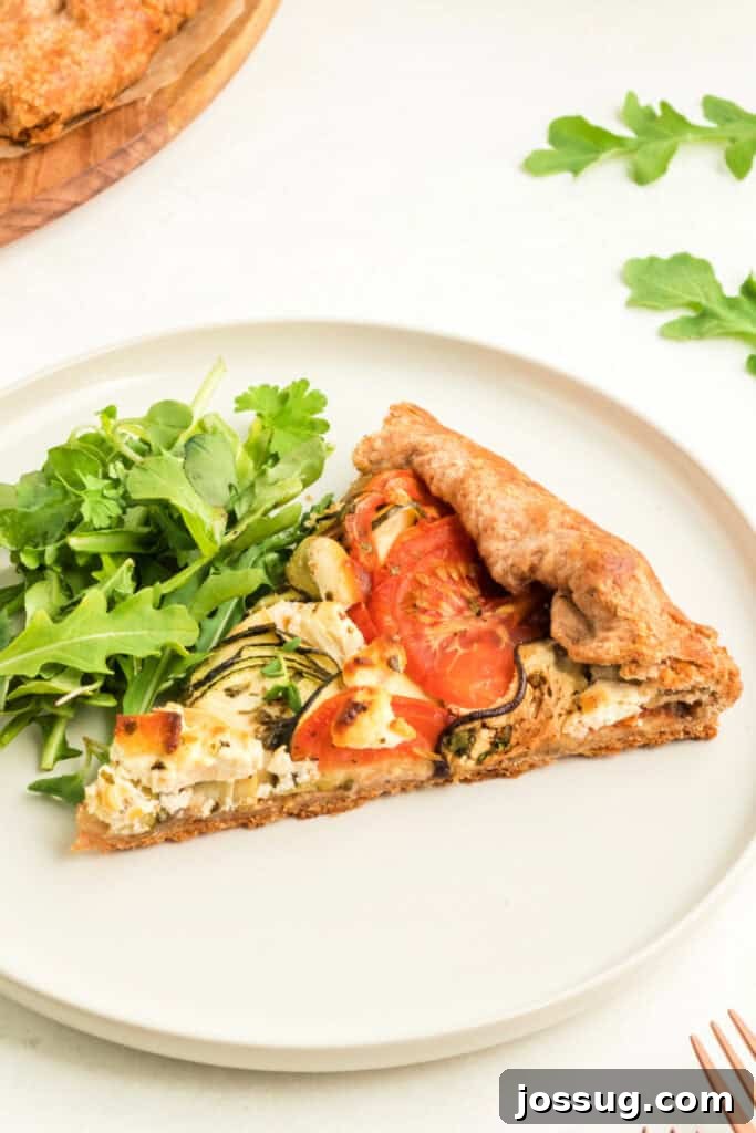 A perfectly baked slice of summer vegetable galette, displaying its golden crust and colorful vegetable filling, elegantly served with a side of fresh green salad on a white plate.