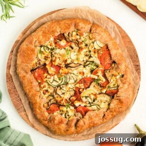 Overhead view of summer vegetable galette on parchment-lined wooden board, ready to serve.