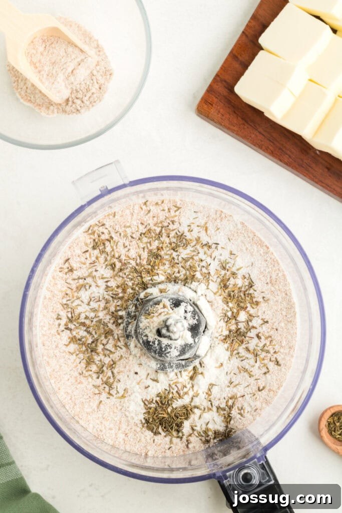 Food processor bowl containing a blend of whole wheat flour, all-purpose flour, kosher salt, and dried thyme, ready for butter.