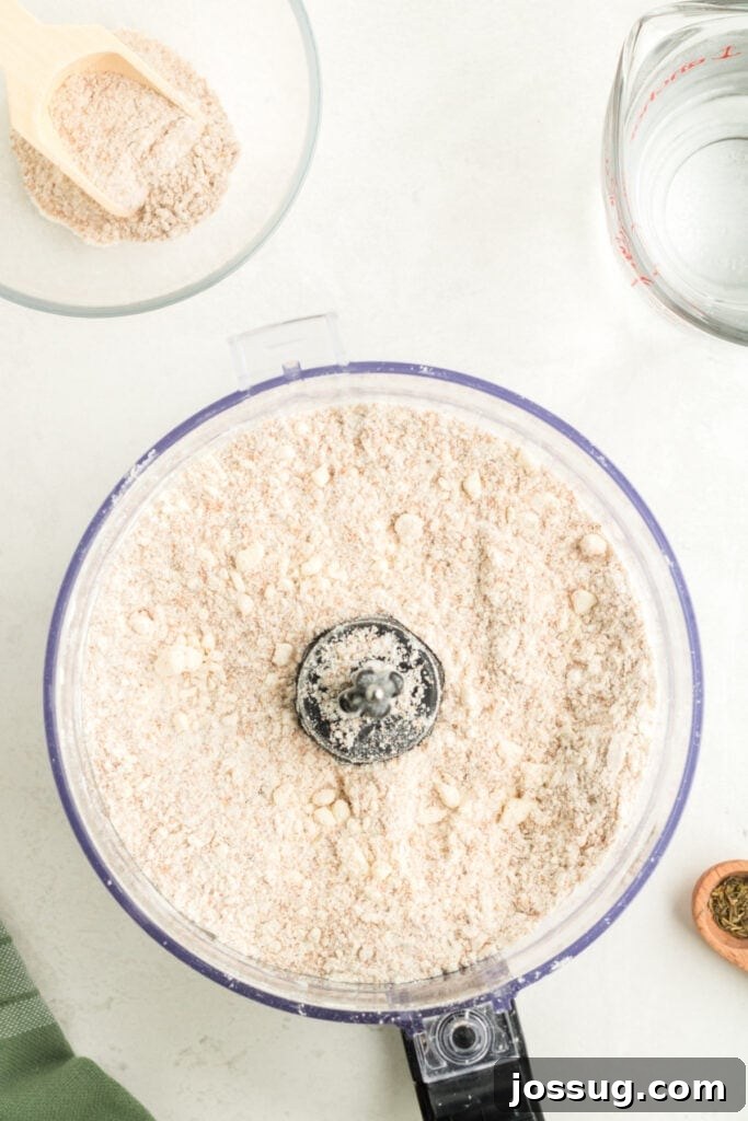 Close-up of flour and cold butter mixed into coarse, pea-sized crumbs in a food processor, essential for a flaky galette crust.