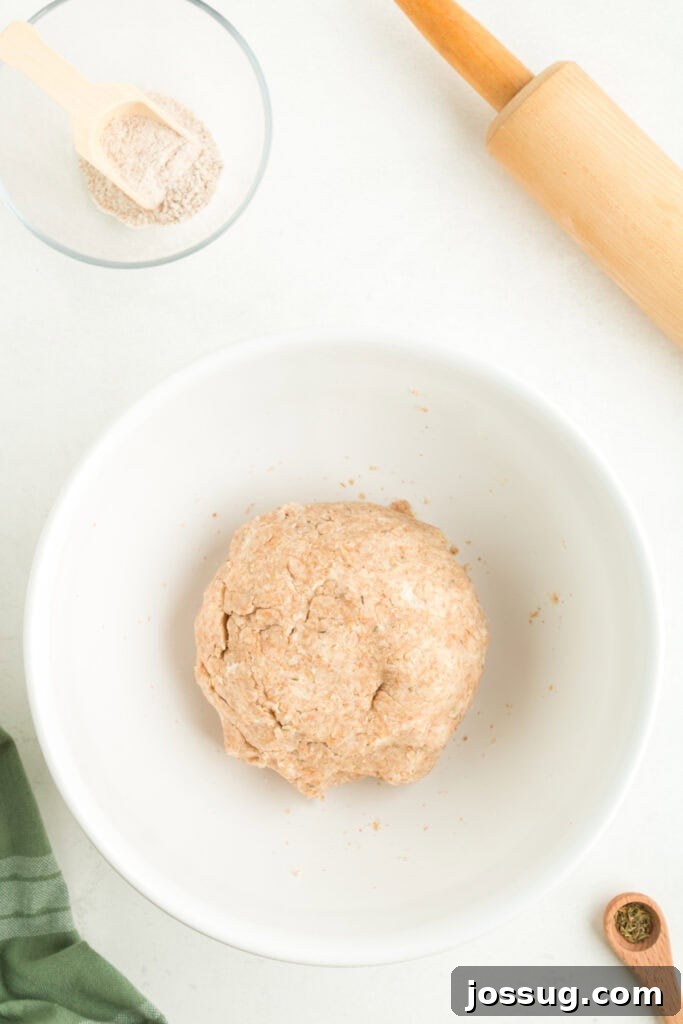 Perfectly formed whole wheat galette dough, shaped into a smooth disk and resting in a white bowl, covered, before chilling.