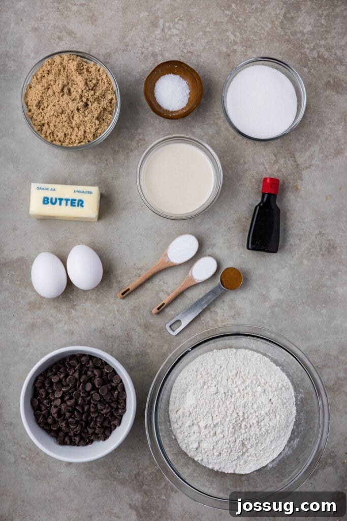 Overhead view of all pre-measured ingredients neatly arranged on a counter: flour, sugar, eggs, vanilla extract, a bowl of brown butter, sourdough discard, and a generous pile of chocolate chips, ready for mixing.