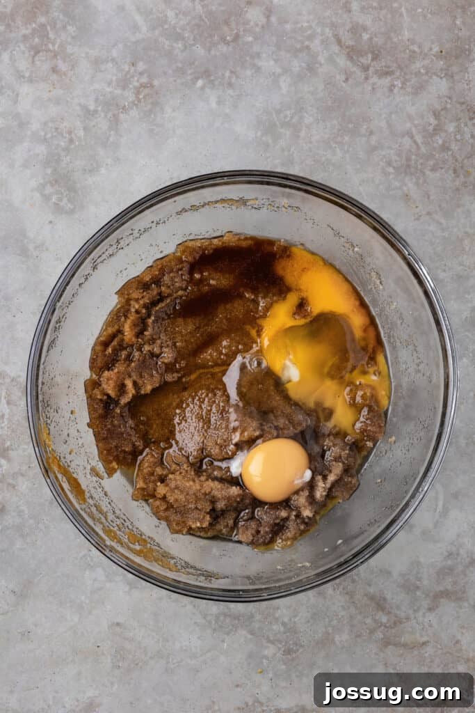 A large egg, an additional egg yolk, and a splash of vanilla extract carefully added to the creamed butter and sugar mixture in a mixing bowl, ready for whisking.