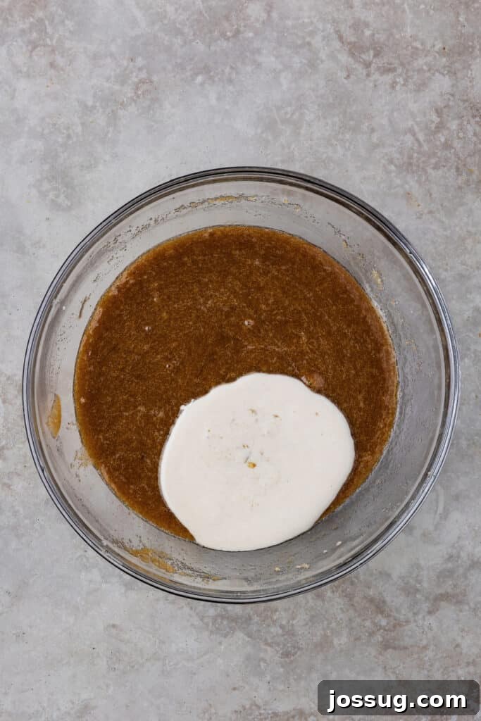 A generous scoop of room-temperature sourdough discard freshly added to the creamy wet batter in the mixing bowl, showing its thick, slightly bubbly consistency.