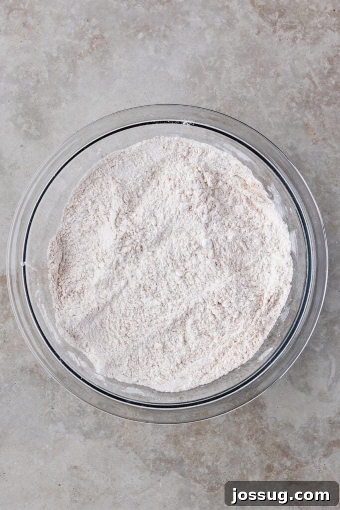 A separate bowl holds the perfectly combined dry ingredients: all-purpose flour, baking soda, baking powder, salt, and ground cinnamon, whisked to ensure even distribution.