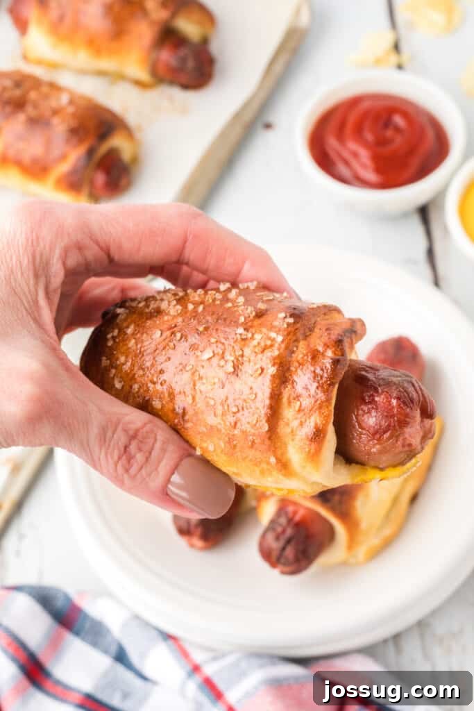 Homemade Pretzel Dogs in a Snap 3 A hand holding a perfectly baked, golden brown pretzel dog, showing its soft texture.