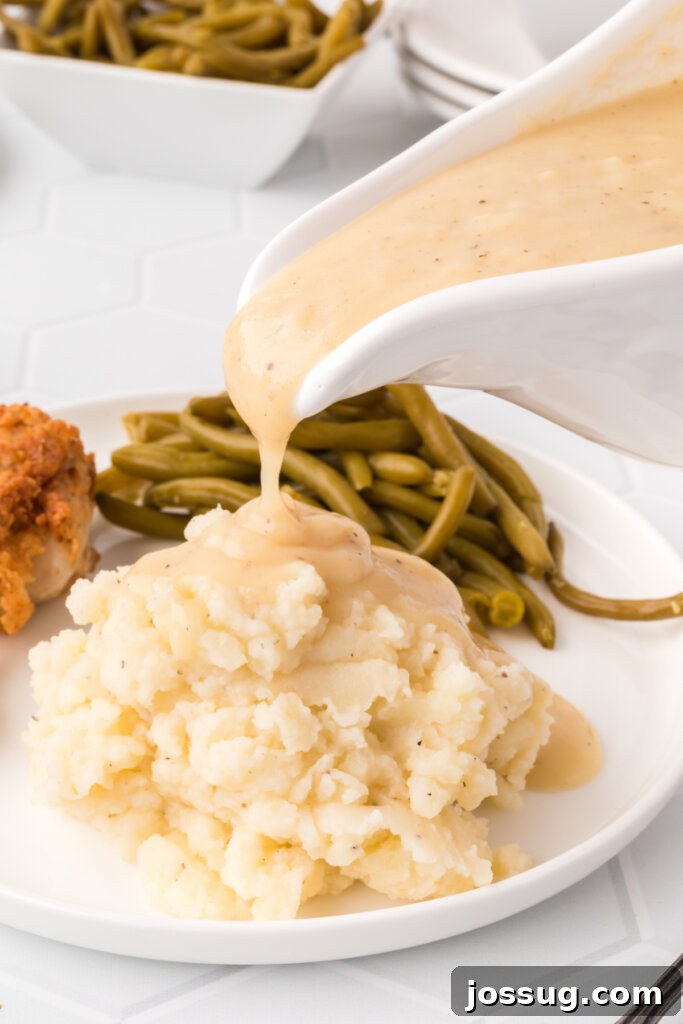 Mastering the Art of Gravy 2 Rich chicken gravy being generously poured over a serving of creamy mashed potatoes, ready to be enjoyed.