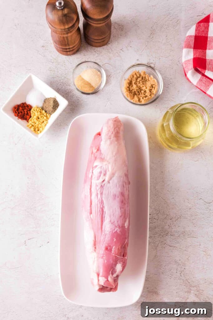 Overhead view of raw pork tenderloin on a white tray surrounded by rub ingredients and olive oil