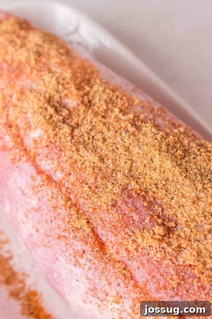 Pork tenderloin coated with dry rub seasoning on a white tray