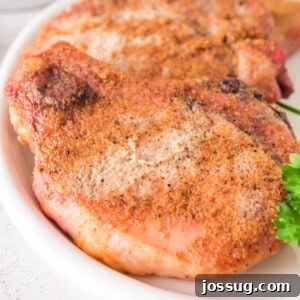 Effortlessly Delicious Smoked Pork Chops 10 Close-up of juicy smoked pork chops with a crispy rub, served on a white plate with parsley garnish, highlighting their golden crust and tender appearance.