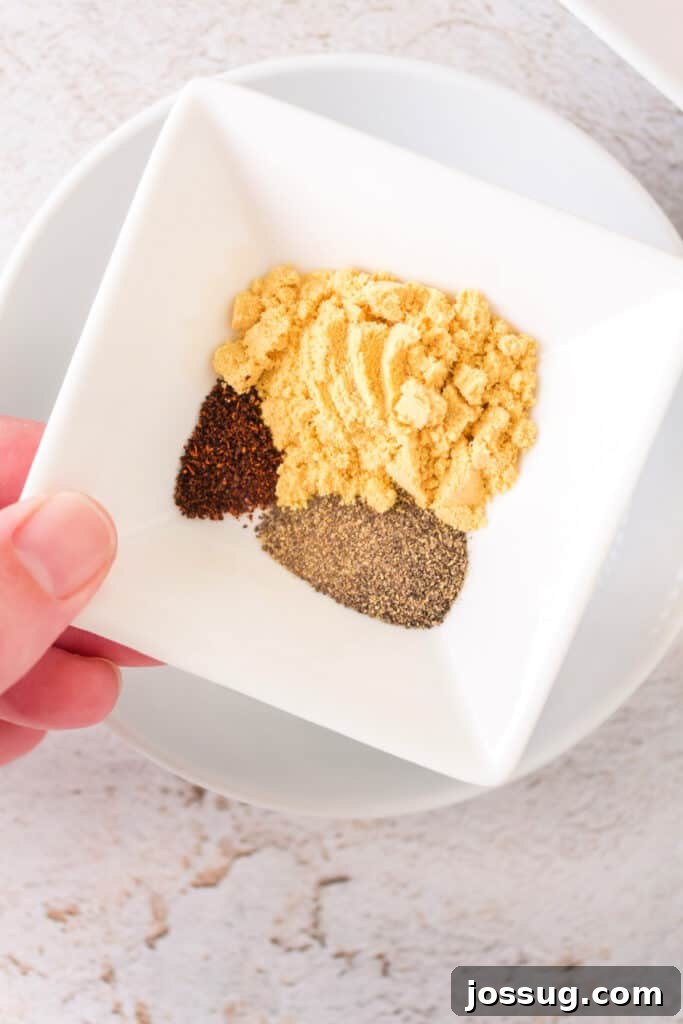 Effortlessly Delicious Smoked Pork Chops 4 Close-up of a small white bowl containing a vibrant mixture of ground mustard, ground black pepper, and chili powder, ready to be blended for the dry rub.
