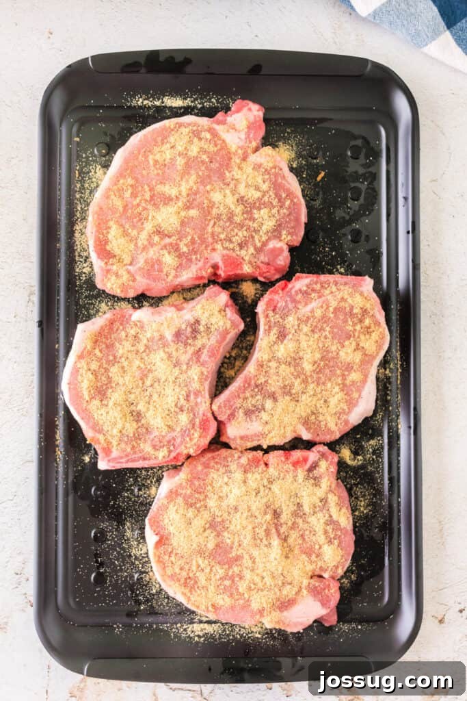Effortlessly Delicious Smoked Pork Chops 7 Four raw pork chops, generously coated with a savory dry rub, are neatly arranged on a black serving tray, ready for the smoker.