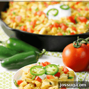 Fiesta Mac & Cheese on a white plate with a skillet and fresh vegetables.