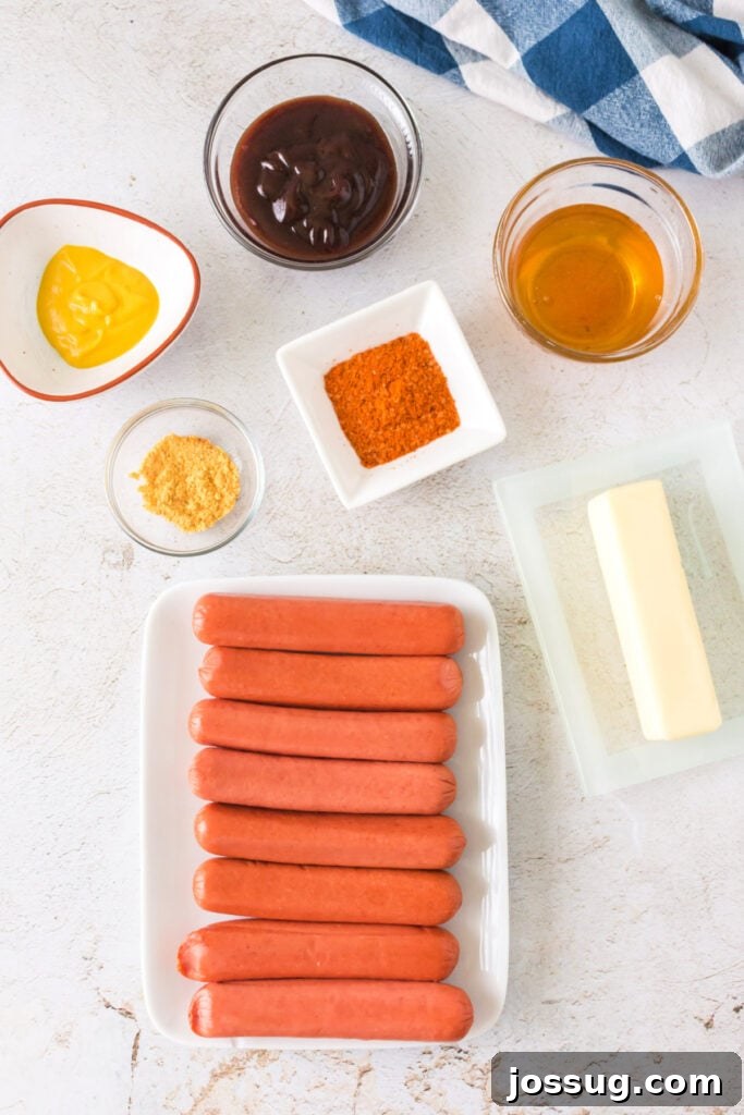 Overhead view of ingredients including hot dogs, butter, mustard, BBQ sauce, honey, and spices on a white surface
