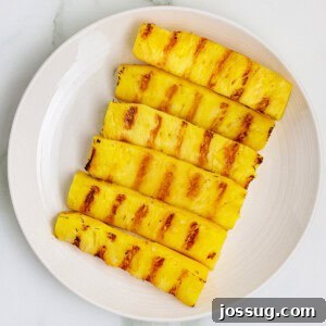 Square crop of grilled pineapple spears with charred grill marks on a white plate