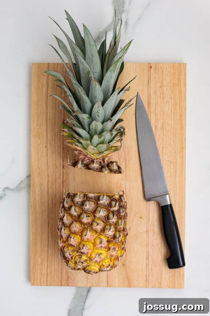 Pineapple with top removed on a cutting board next to a chef’s knife