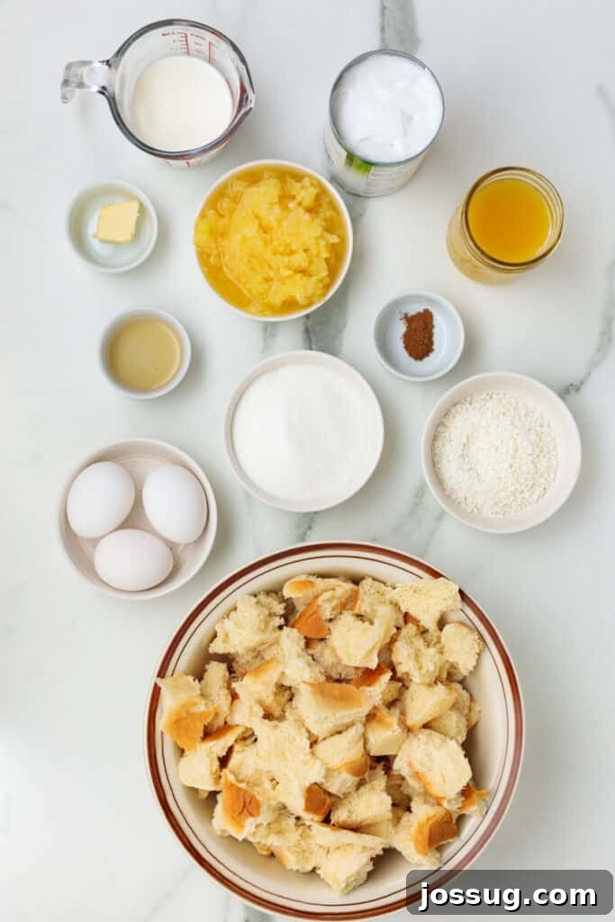 Caribbean Piña Pudding Bake 3 Overhead shot of all measured ingredients laid out for making Piña Colada Bread Pudding, including torn Hawaiian rolls, pineapple juice, coconut milk, sugar, eggs, and shredded coconut.