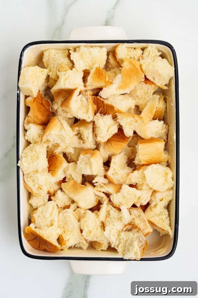 Caribbean Piña Pudding Bake 5 Torn sweet Hawaiian rolls meticulously arranged in a greased rectangular baking dish, ready to be soaked in the rich custard mixture for Piña Colada Bread Pudding.