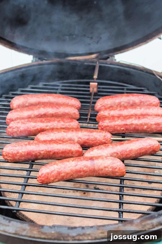 Bratwursts gently browning and smoking on the grill within the confines of a smoker, nearing completion.
