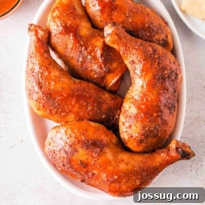 Top-down view of glazed smoked chicken leg quarters arranged in a white oval dish, perfectly cooked and ready to serve.