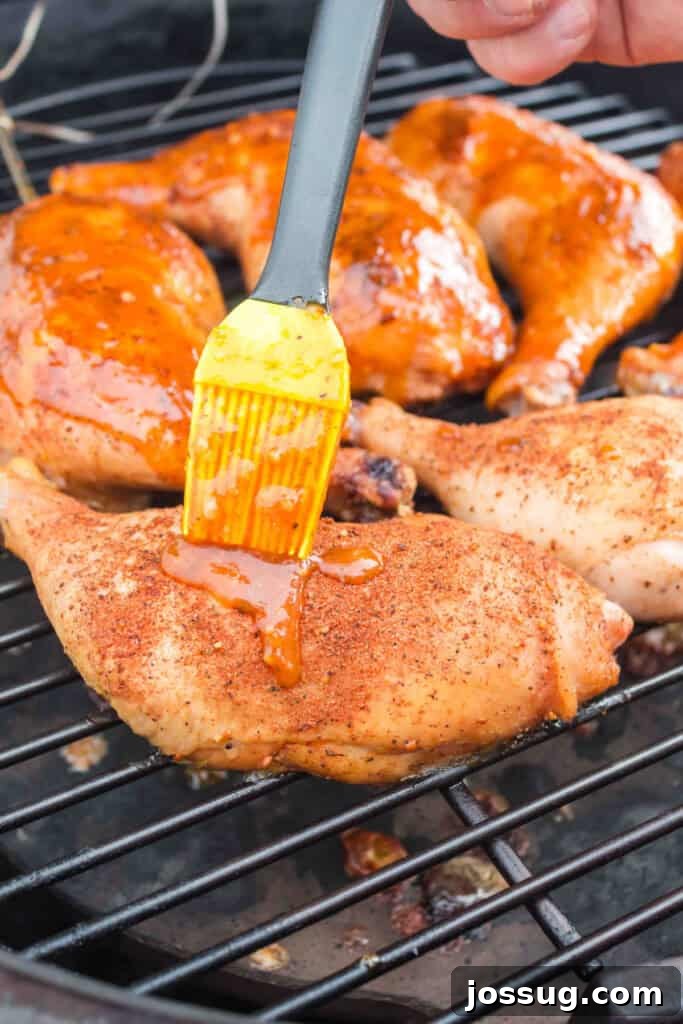 Succulent Smoked Chicken Legs 7 Chicken quarters on the smoker grill being brushed with the thick, sweet, and smoky BBQ glaze during the final stage of cooking.