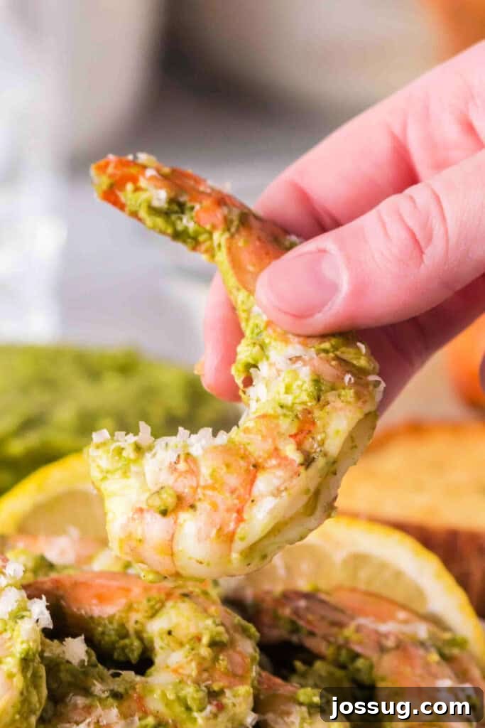 Zesty Grilled Pesto Shrimp 2 Hand holding a single grilled pesto shrimp, topped with cheese, against a blurred background.