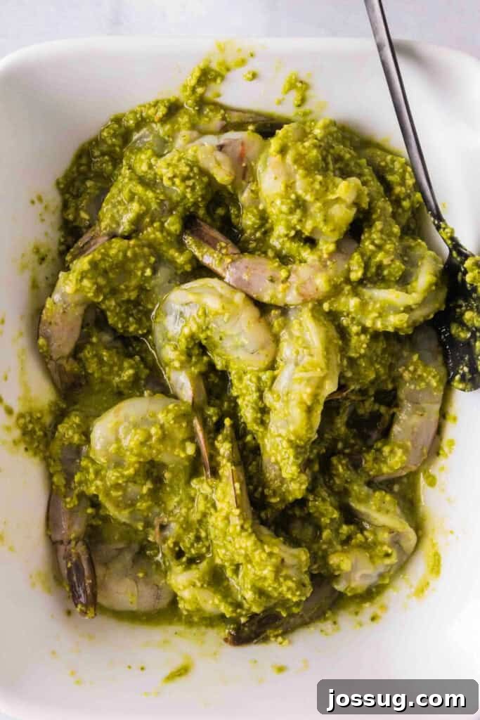 Zesty Grilled Pesto Shrimp 4 Shrimp coated in bright green basil pesto marinade in a bowl with a spoon, ready for grilling.