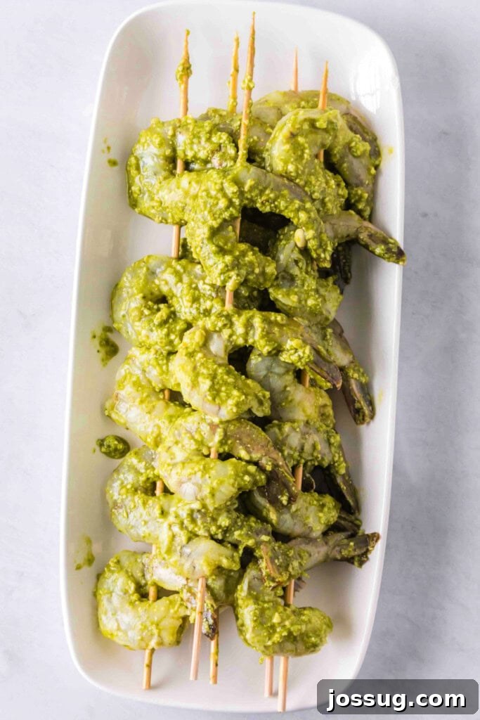 Zesty Grilled Pesto Shrimp 5 Shrimp skewered and coated in pesto, arranged neatly on a white platter before cooking.