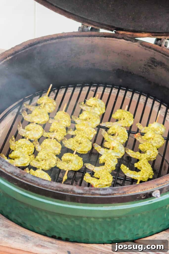 Zesty Grilled Pesto Shrimp 6 Shrimp skewers placed on a smoky grill, just beginning to cook and acquire char marks.