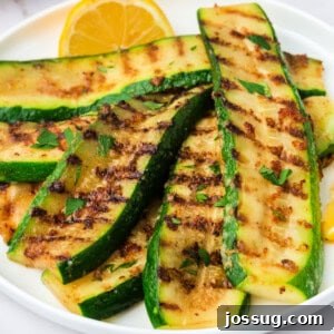 Close-up of grilled zucchini slices with melted parmesan and grill marks, garnished with parsley and lemon.
