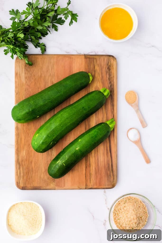Whole zucchinis on a wooden cutting board with fresh parsley, a bowl of melted butter, garlic powder, salt, grated parmesan, and Italian breadcrumbs, ready for recipe preparation.