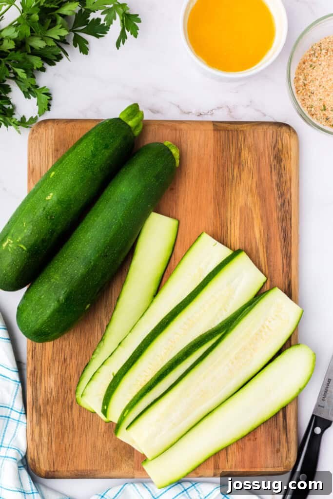 Zucchinis partially sliced into long, uniform strips on a wooden cutting board with prep ingredients nearby.