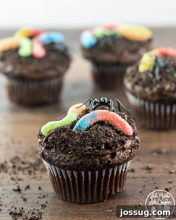 Delicious dirt cupcakes, topped with crushed cookies and gummy worms, presented on a cutting board.