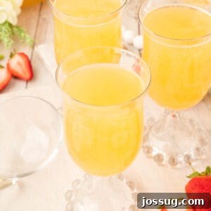 Square crop showing three glasses of golden mock champagne punch on a light wood table with strawberries scattered nearby.