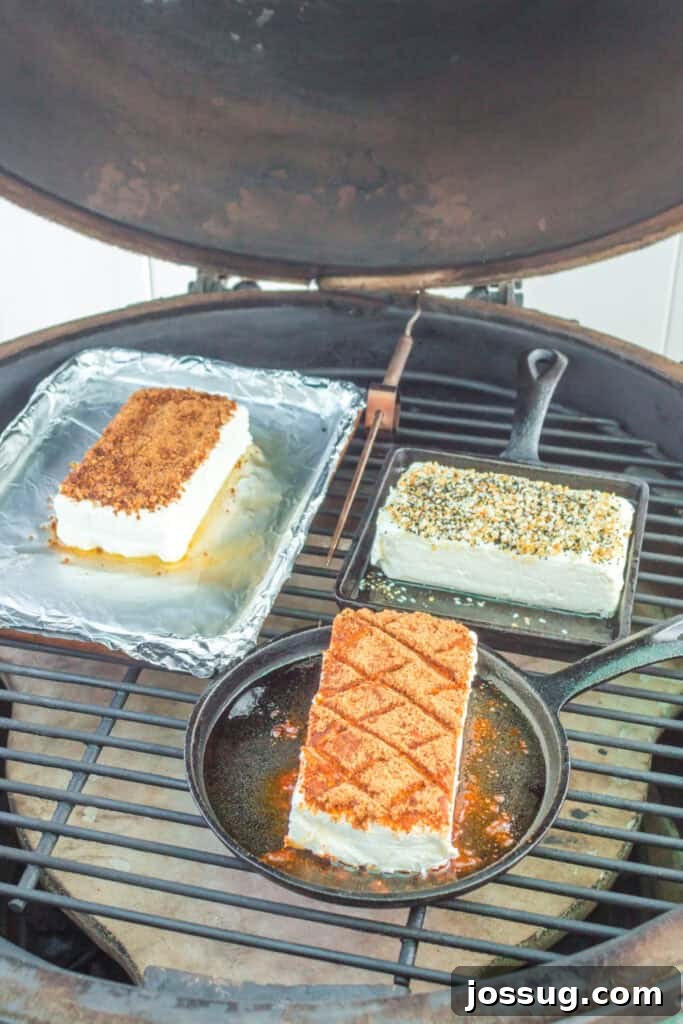 Three cream cheese blocks smoking on a grill in various pans
