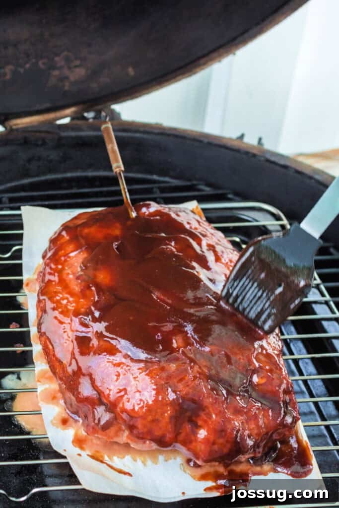 Pit Smoked Meatloaf 9 A basting brush applying a rich, glossy layer of BBQ sauce over the smoking meatloaf, creating a beautiful glaze during the cooking process.