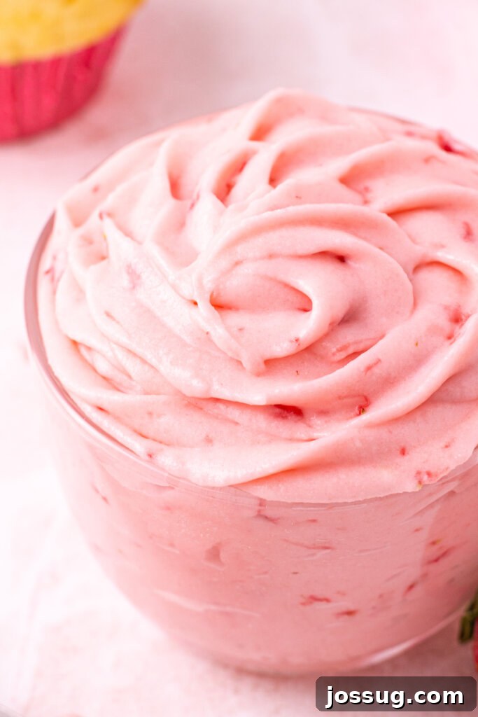 Velvet Strawberry Buttercream 2 Close-up of a jar filled with vibrant, creamy homemade strawberry buttercream frosting, garnished with a fresh strawberry