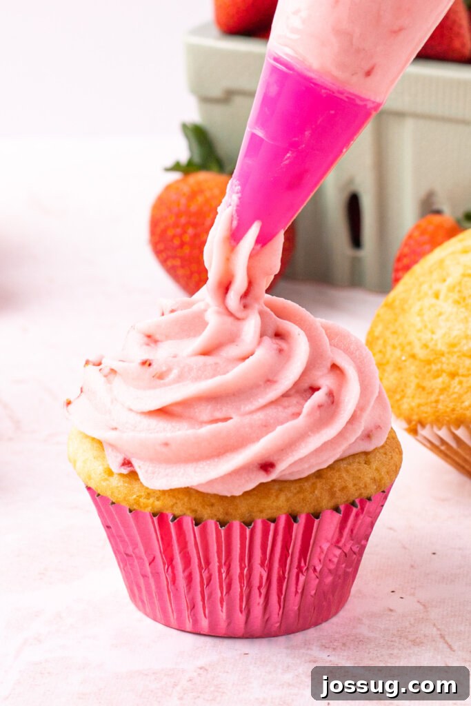 Velvet Strawberry Buttercream 4 A delicious strawberry buttercream frosting being skillfully piped onto a cupcake, demonstrating a perfect, fluffy swirl