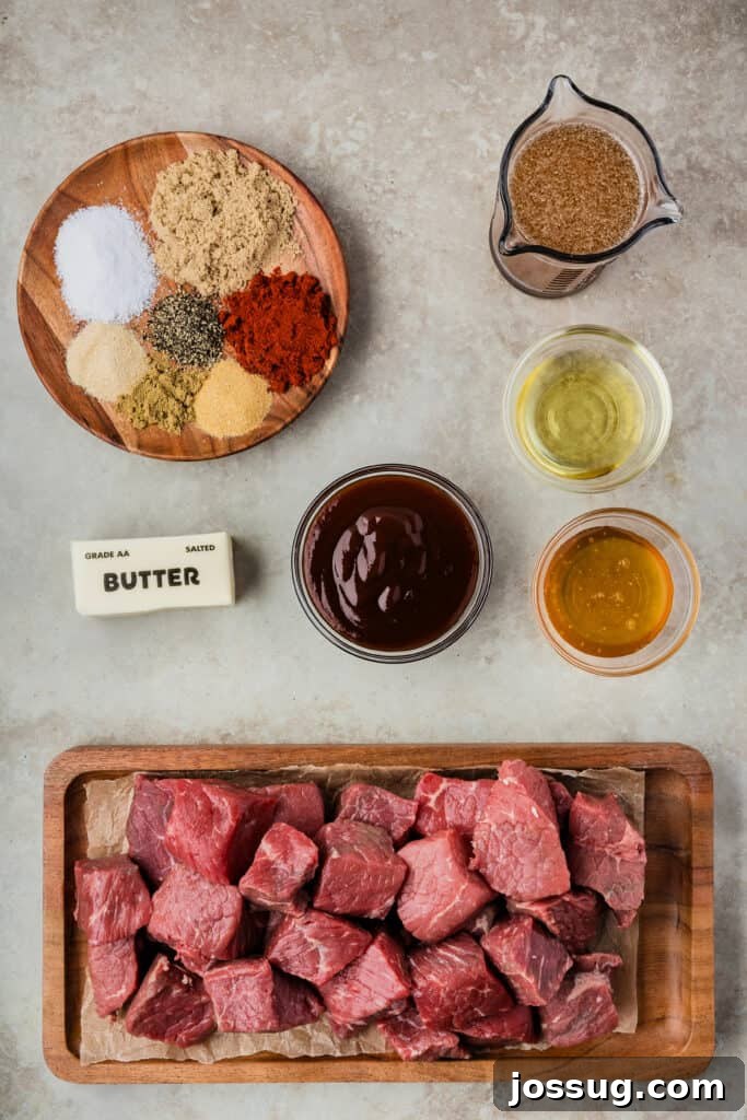 Burnt Ends on a Budget 3 Overhead shot of ingredients for Poor Man’s Burnt Ends, including raw chuck roast, various spices for the rub, butter, beef broth, honey, and a bottle of BBQ sauce, all arranged on a rustic wooden surface.