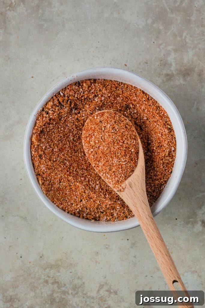 Burnt Ends on a Budget 4 Bowl of homemade BBQ dry rub with a wooden spoon on a neutral countertop, showcasing the rich blend of spices.