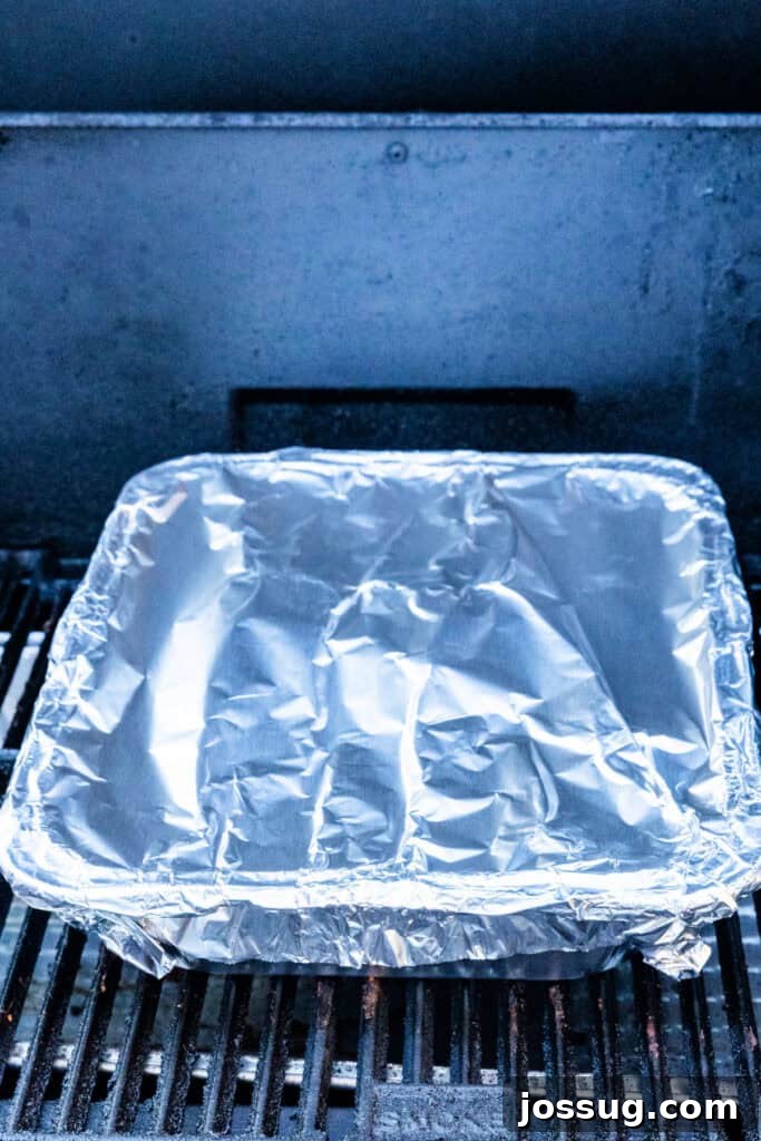 Burnt Ends on a Budget 8 Foil pan tightly covered with aluminum foil on the smoker, ensuring a moist braising environment.