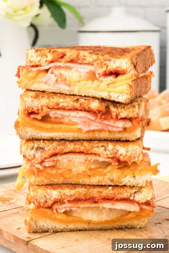 Aloha Grilled Cheese 2 Hawaiian Pizza Grilled Cheese Sandwiches sliced in half and stacked on a cutting board, showcasing melted cheese, Canadian bacon, and pineapple