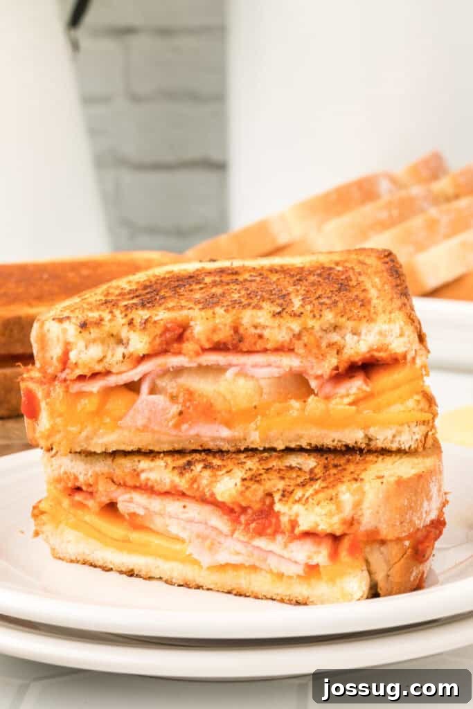 Aloha Grilled Cheese 4 A Hawaiian Pizza Grilled Cheese Sandwich sliced in half and stacked together on a plate, revealing the melted cheese, Canadian bacon, and pineapple filling