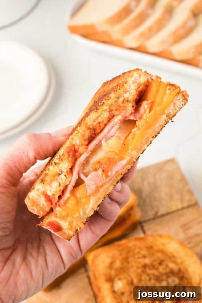 Aloha Grilled Cheese 5 A hand holding half of a Hawaiian Pizza Grilled Cheese Sandwich, showcasing the golden-brown bread and the gooey interior