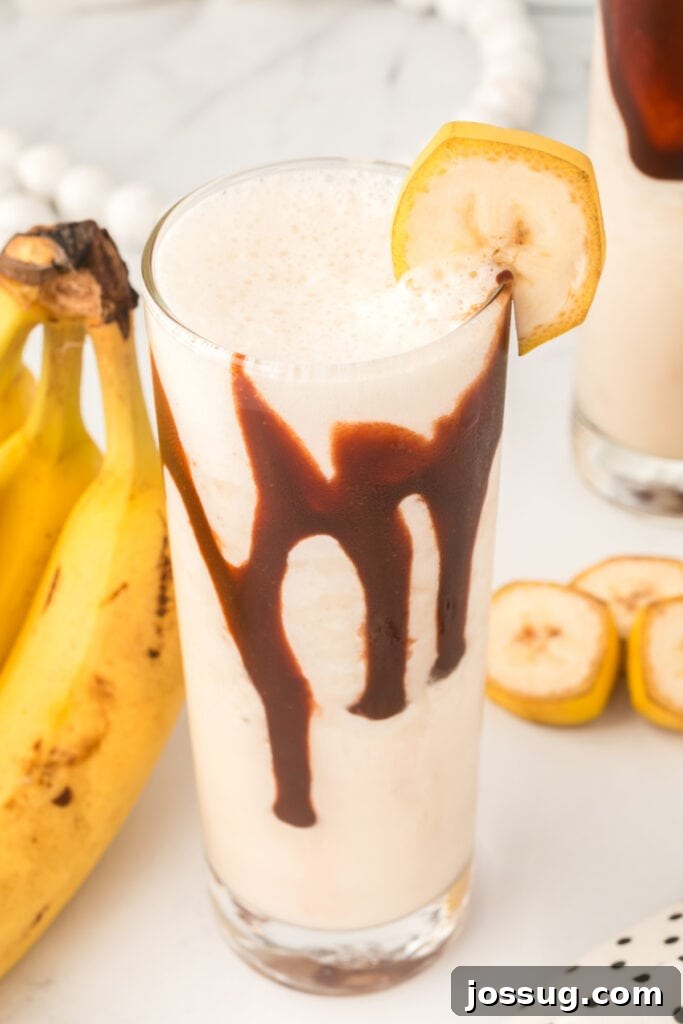Dirty Banana Cocktail served in a tall Collins glass with a luscious chocolate drizzle and a fresh banana slice garnish, evoking tropical vibes.