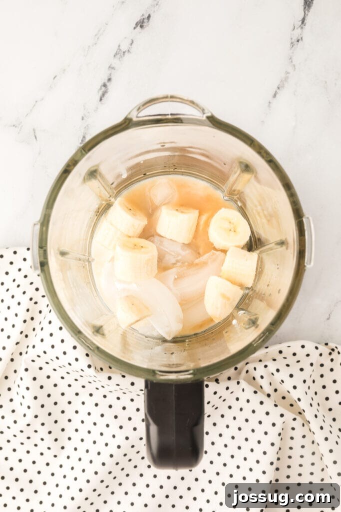 Close-up of ice cubes, sliced banana chunks, and all liquid cocktail ingredients carefully placed inside a blender jar, ready for blending.