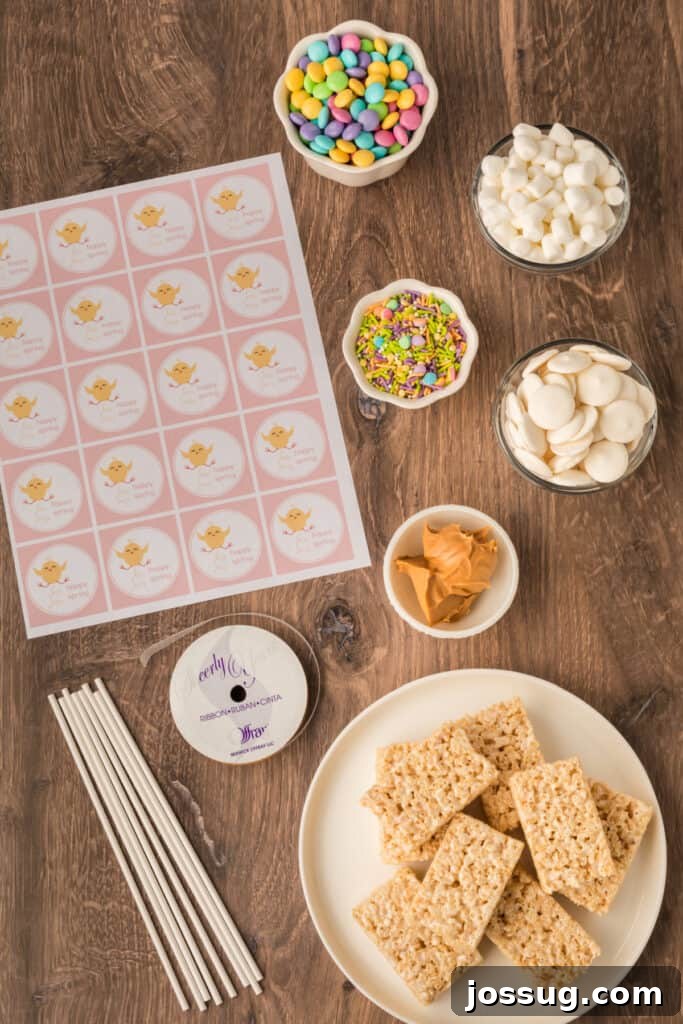 A collection of ingredients laid out on a clean surface, including unwrapped Rice Krispies treats, mini marshmallows, peanut butter, white candy melts, various sprinkles, and spring-colored M&M’s, ready to make Spring Rice Krispies Treats Pops.